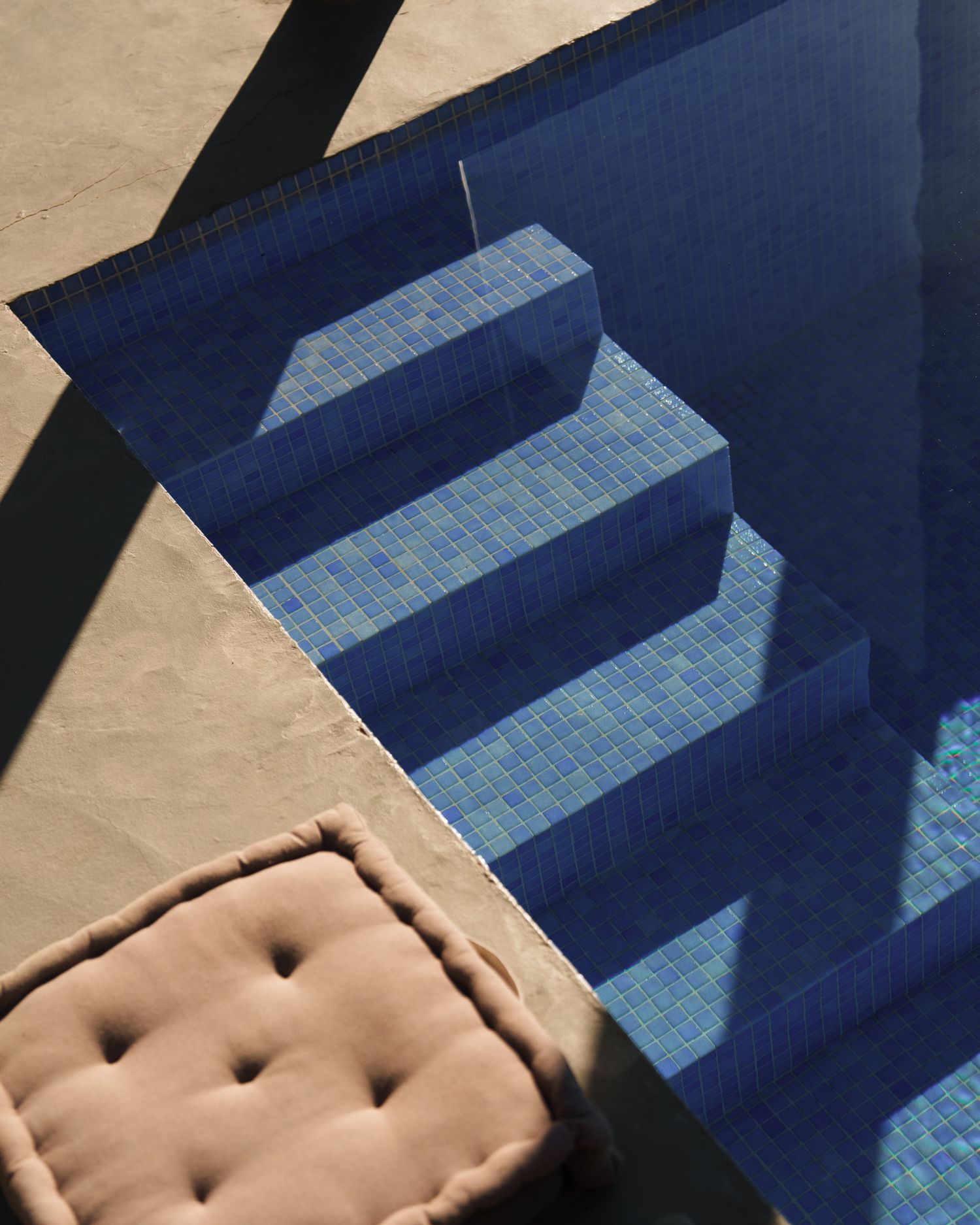 Geometric shadows cast across blue tiled steps with a beige cushioned seat visible in the corner.
