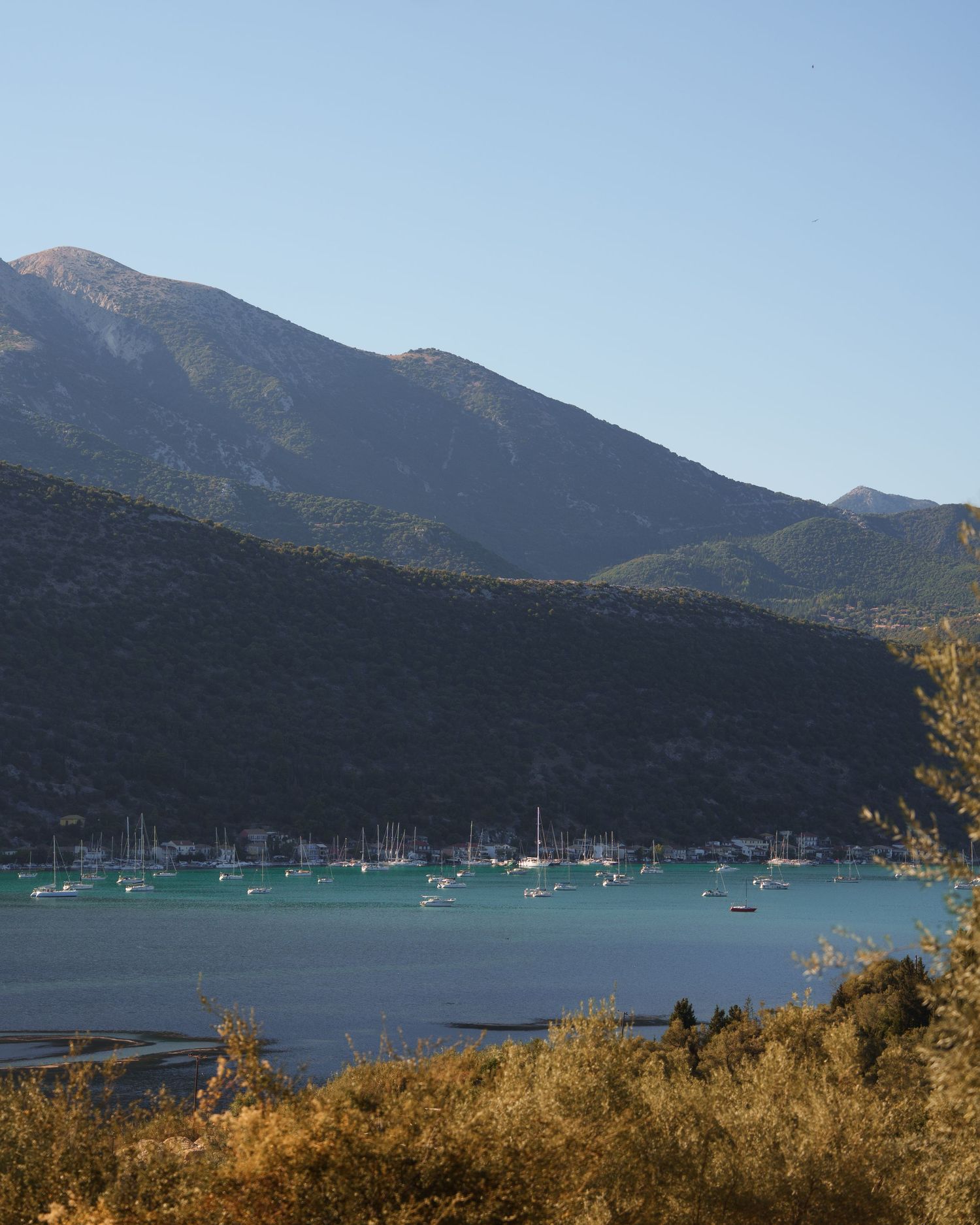 Panoramic view of sailboats anchored in a tranquil mountain lake surrounded by rugged peaks at sunset.