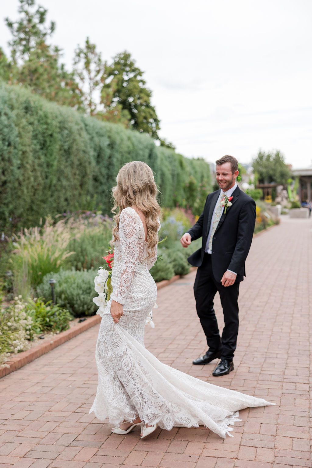 Bride and groom share a playful moment twirling on a brick pathway surrounded by lush garden landscaping.