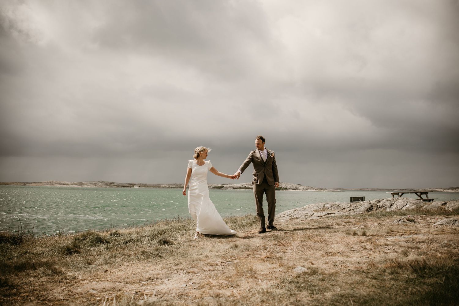 A romantic coastal wedding photoshoot featuring a couple embracing on rocky cliffs overlooking the ocean at sunset.