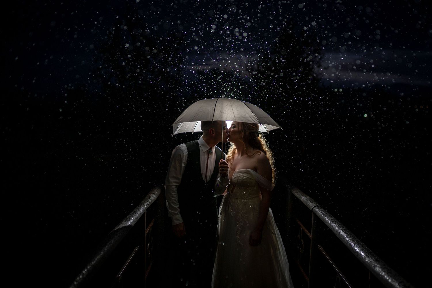 A couple stands under an umbrella at night with a starry sky backdrop creating a romantic silhouette.