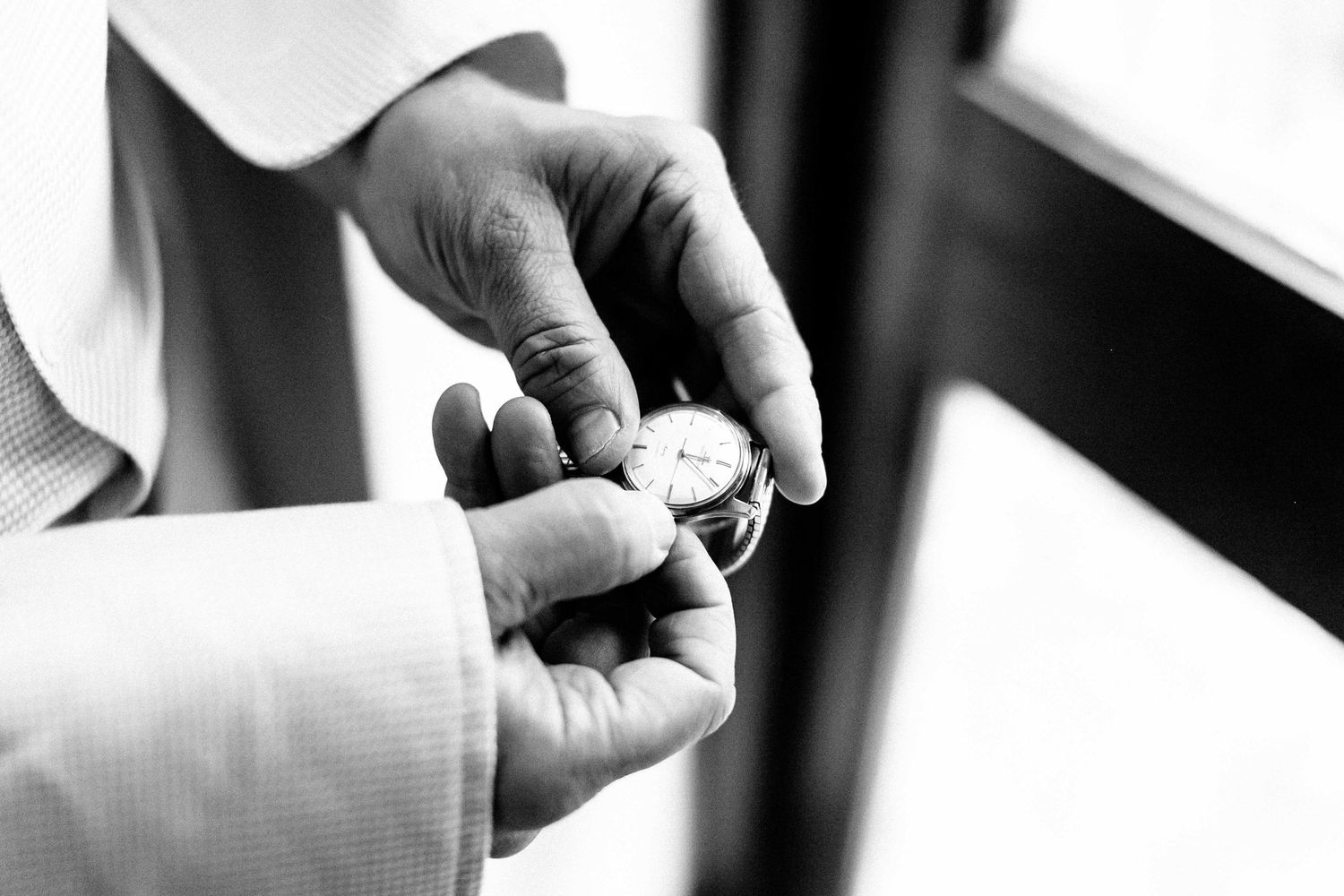 Close-up black and white photo of hands adjusting a suit jacket sleeve and cufflink.