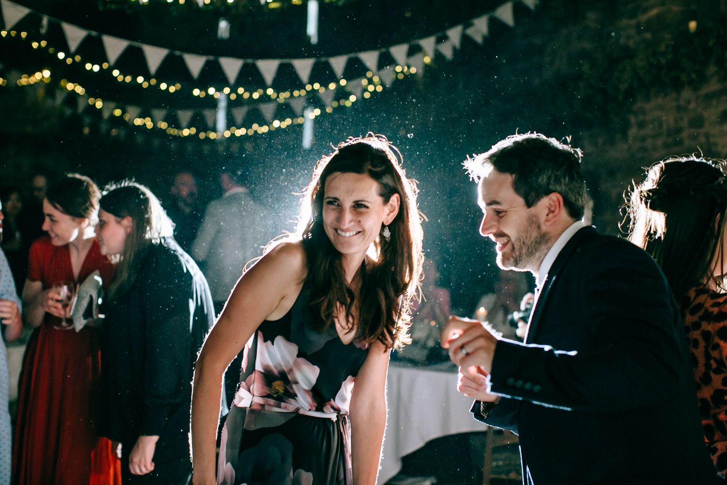 Wedding guests dance and celebrate under twinkling string lights during an evening reception celebration.