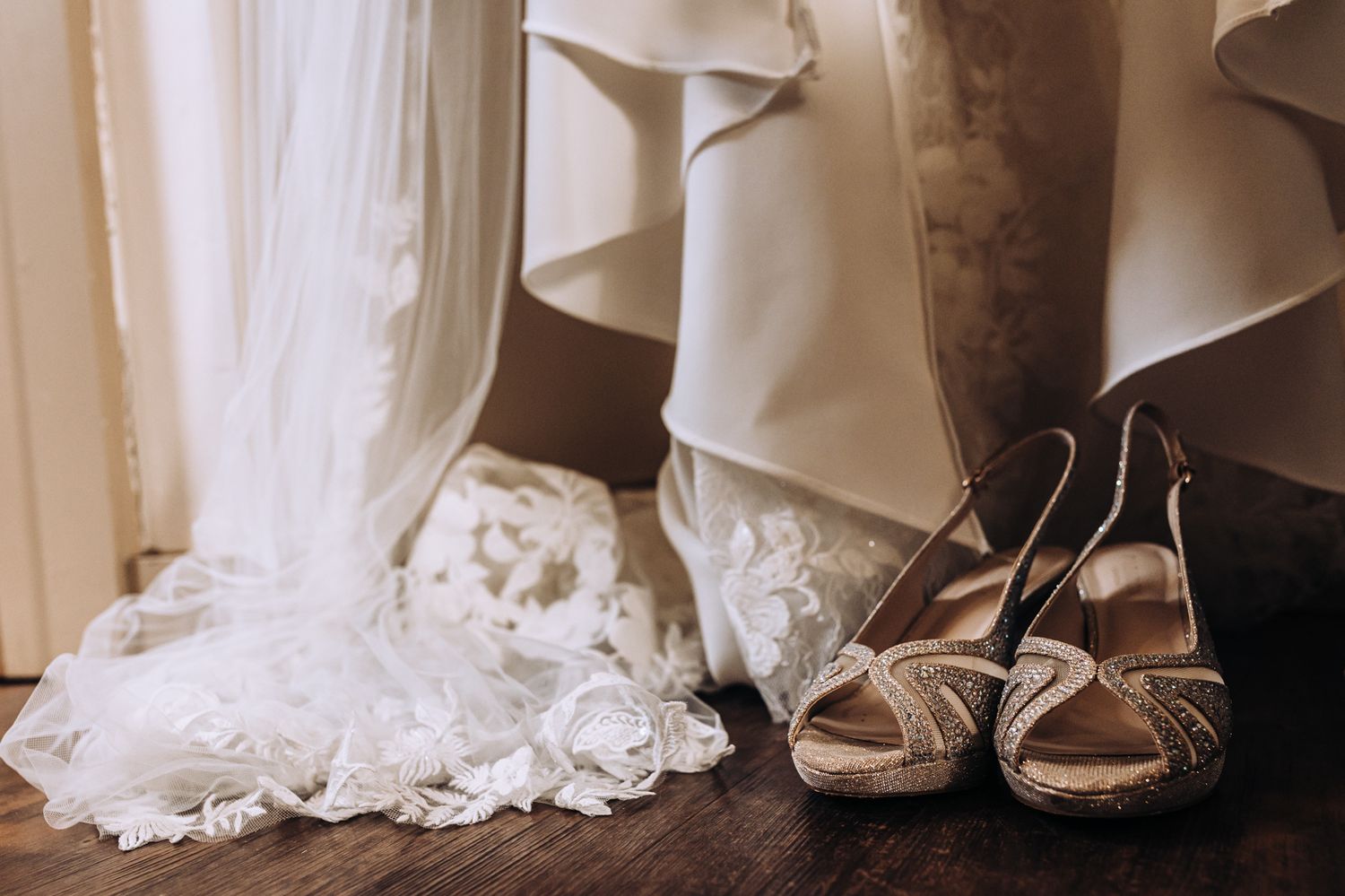 A row of elegant white wedding dresses and shoes displayed on hangers against a light colored wall.