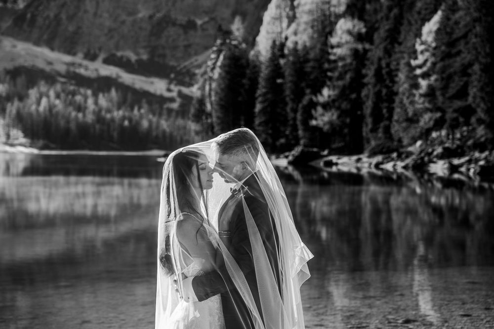 A romantic couple shares an intimate moment during their wedding photoshoot by a serene mountain lake.