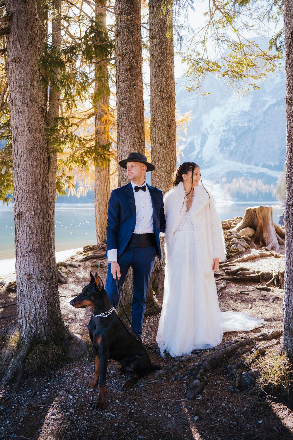 Romantic wedding couple poses together in a forest by a mountain lake during golden hour.