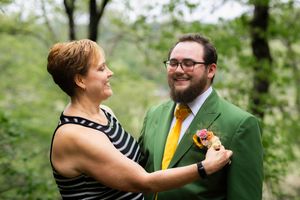 A couple in formal attire shares a tender dance moment outdoors surrounded by lush greenery.