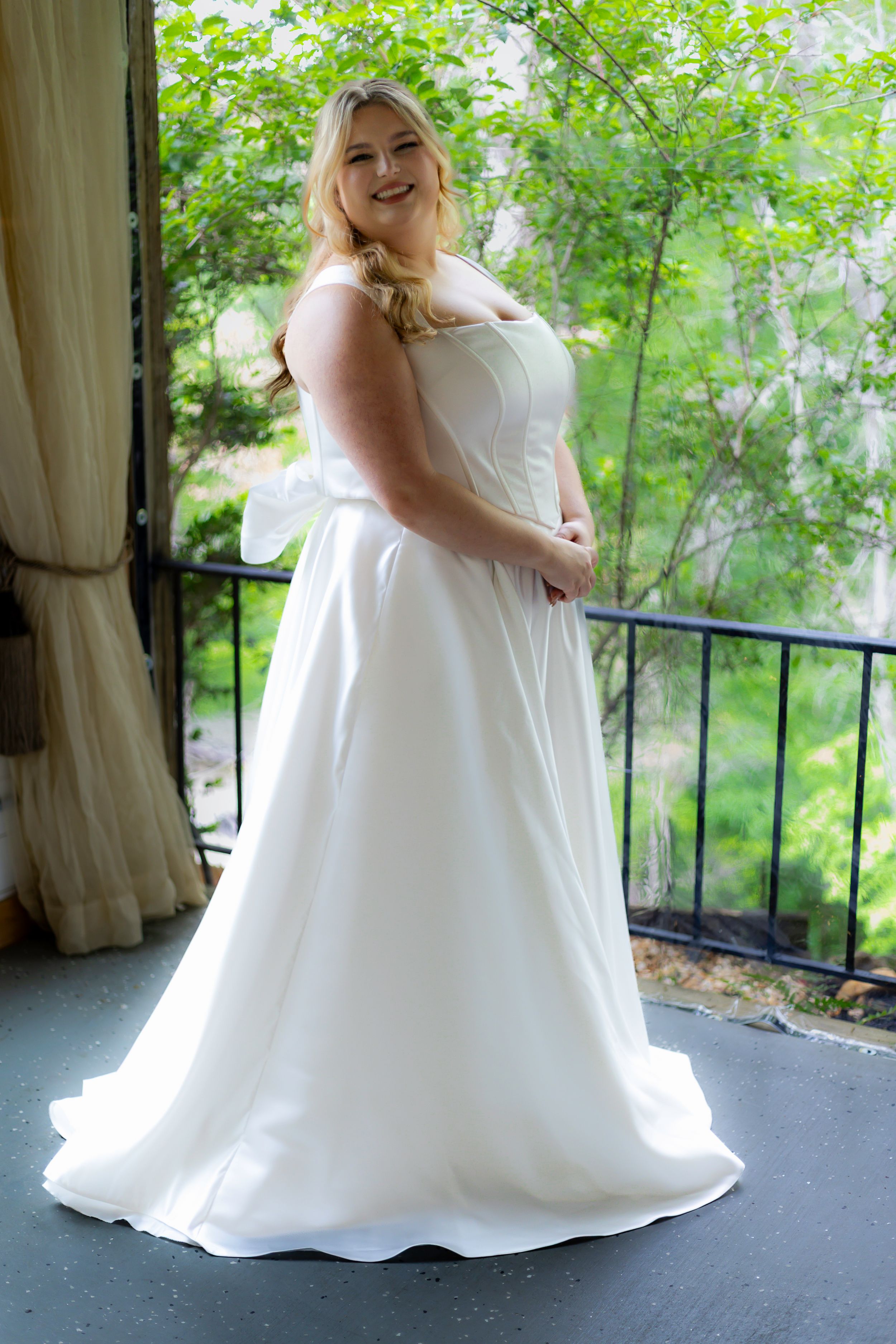 A flowing white wedding dress is showcased in a series of outdoor photos on a balcony surrounded by greenery.