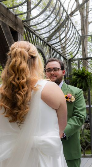 Wedding couple sharing intimate moment under curved wooden pergola with greenery and natural light.