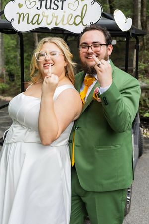 A couple holds 'Just Married' signs while celebrating their wedding day, with one wearing green and one in white.