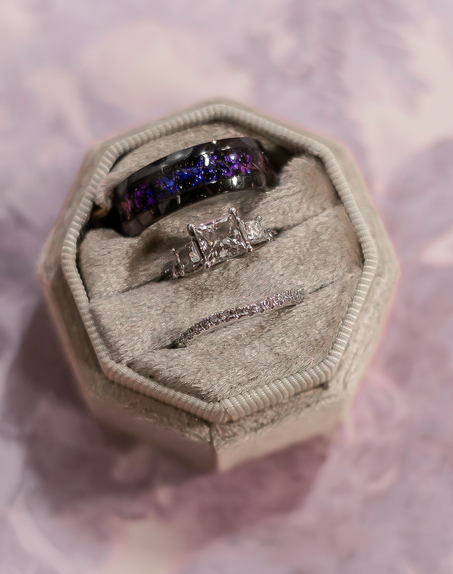 Wedding rings nestled in a beige velvet octagonal ring box featuring a blue galaxy design and diamond accents.