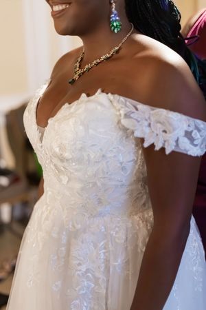 A close-up detail of a white wedding dress showing delicate lace and floral appliques on the bodice.