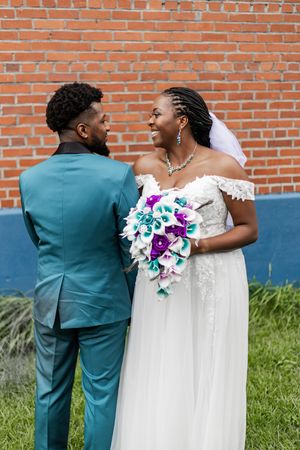 Wedding couple in teal and white attire share intimate moments against brick wall backdrop.