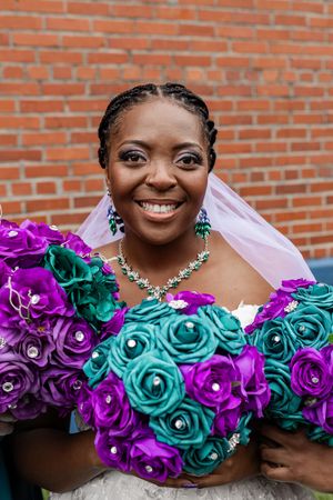 Beautiful wedding bouquet featuring vibrant teal and purple roses with crystal accents against a brick wall background.