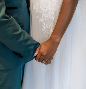 Wedding couple's hands shown in formal attire with elegant white and teal details.