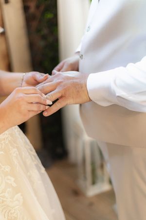Close-up shot of hands exchanging wedding rings during a ceremony, with white attire and delicate details visible.