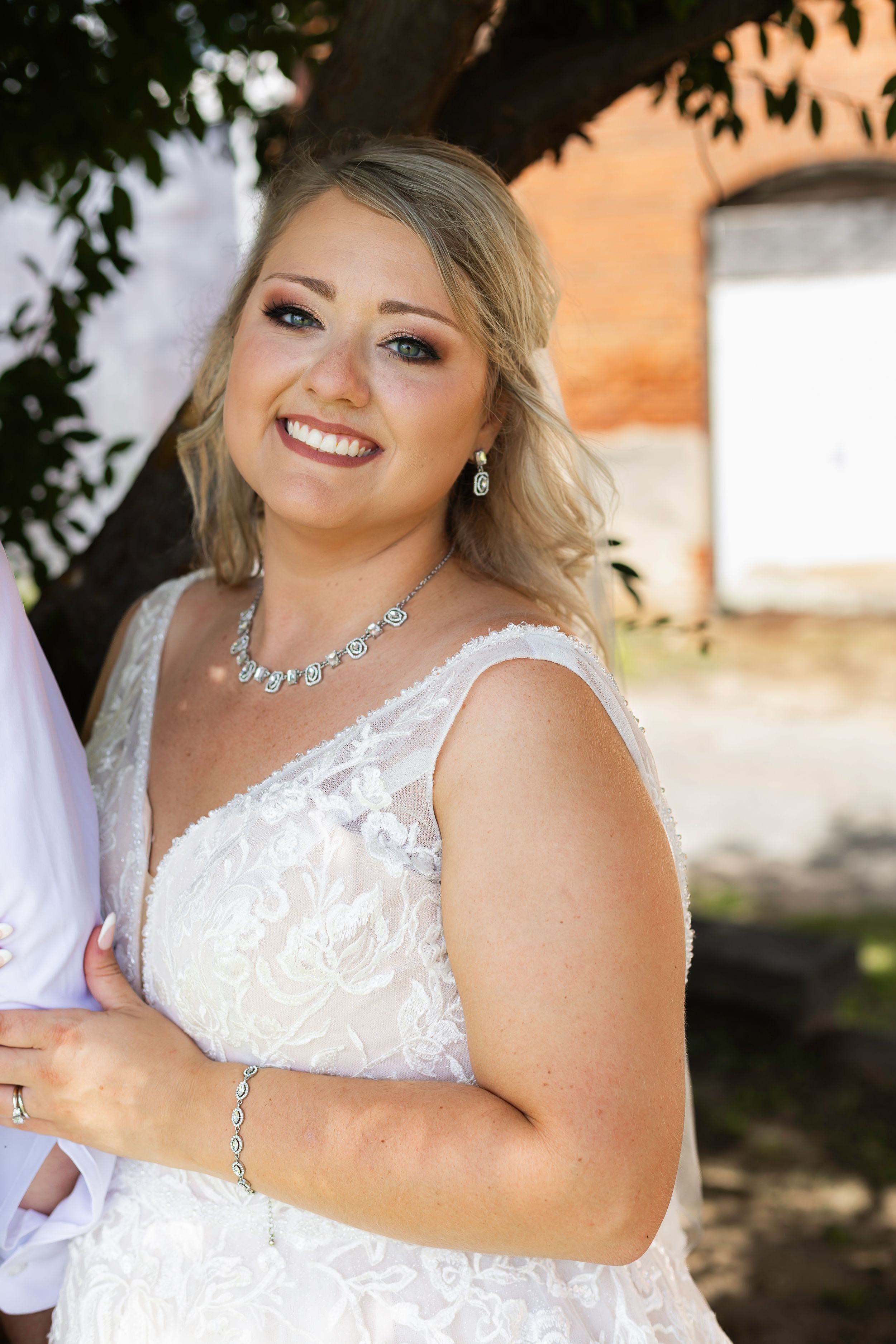 A close up of a formal white dress with lace details and elegant jewelry.