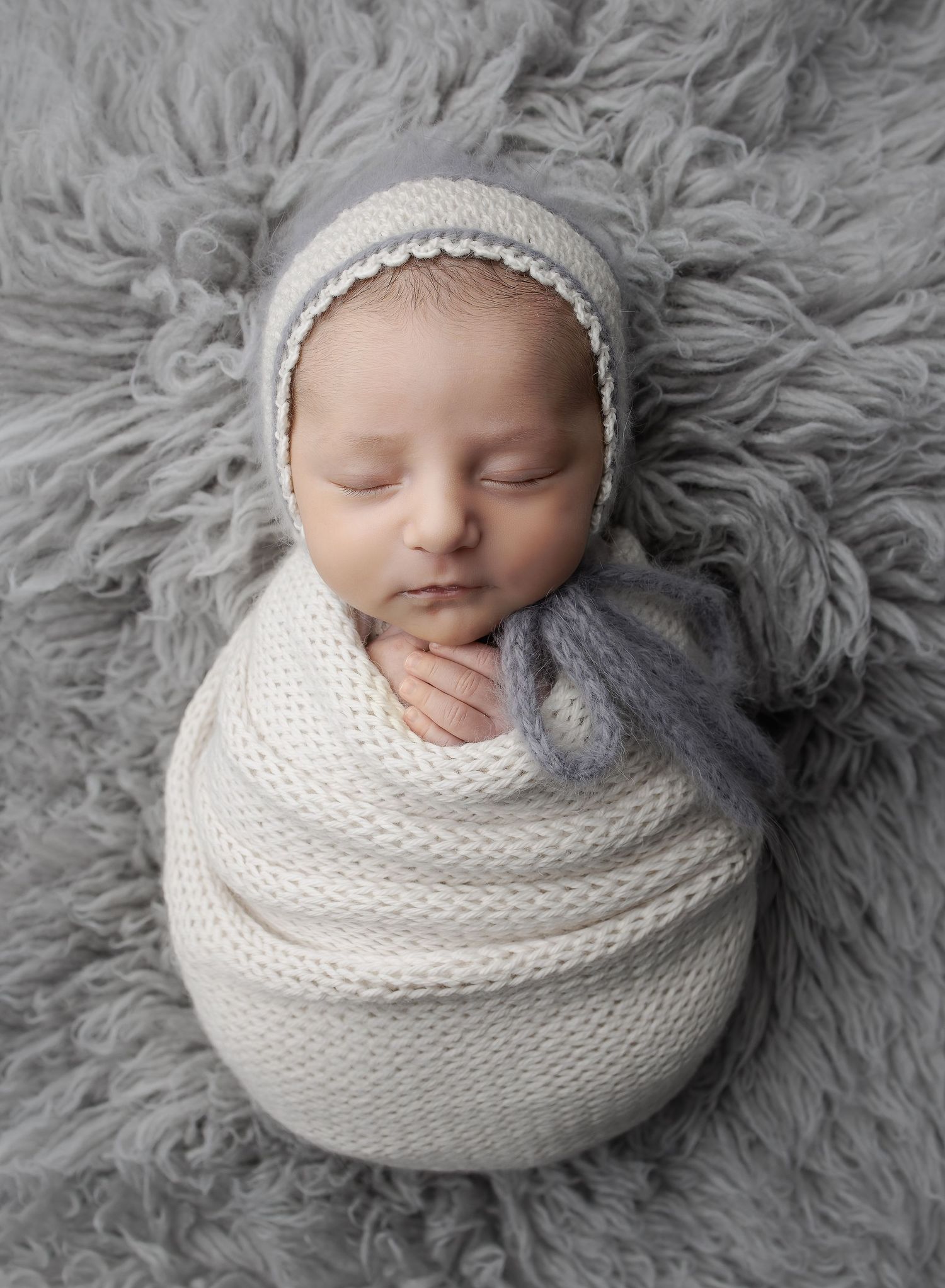 Soft tones Newborn Portrait in gray and cream.  Baby is swaddled in a cream knit wrap and wearing a gray and white bonnet at Austin Studio.