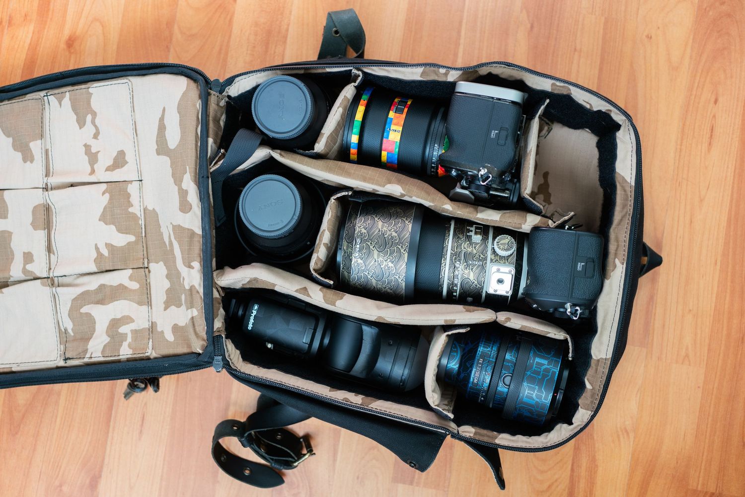 Professional camera equipment and lenses arranged neatly inside a black camera backpack on wooden floor.