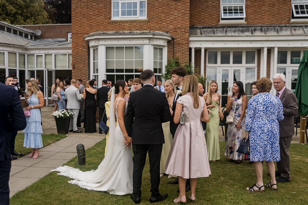 Wedding guests mingling on lawn outside traditional brick venue.
