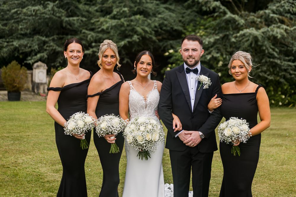 Wedding party in black and white attire posing together on lawn.