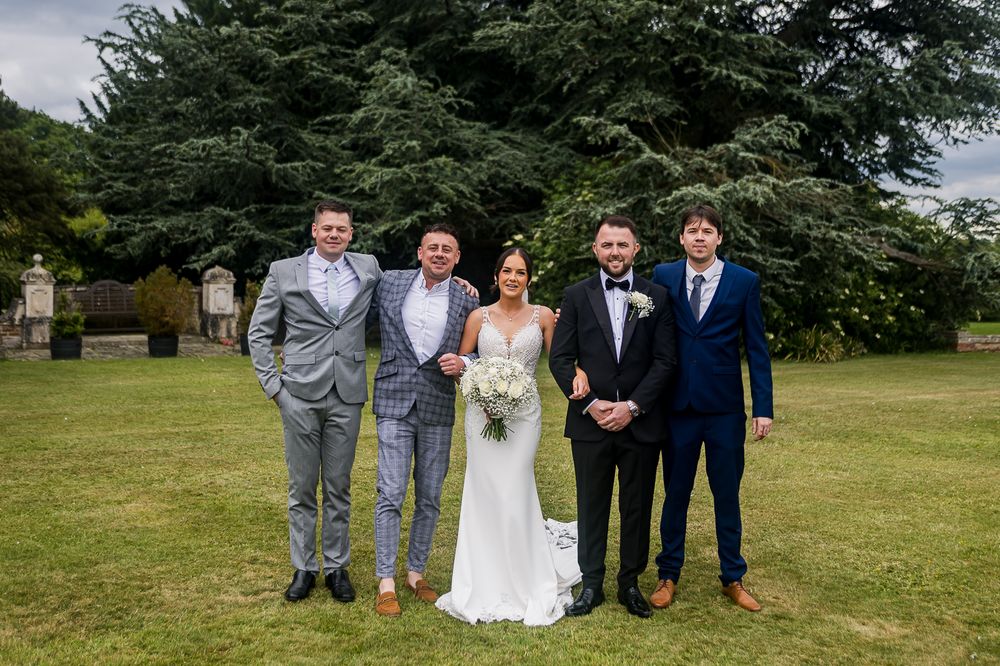 Wedding group photo with mix of formal and casual attire on green lawn.