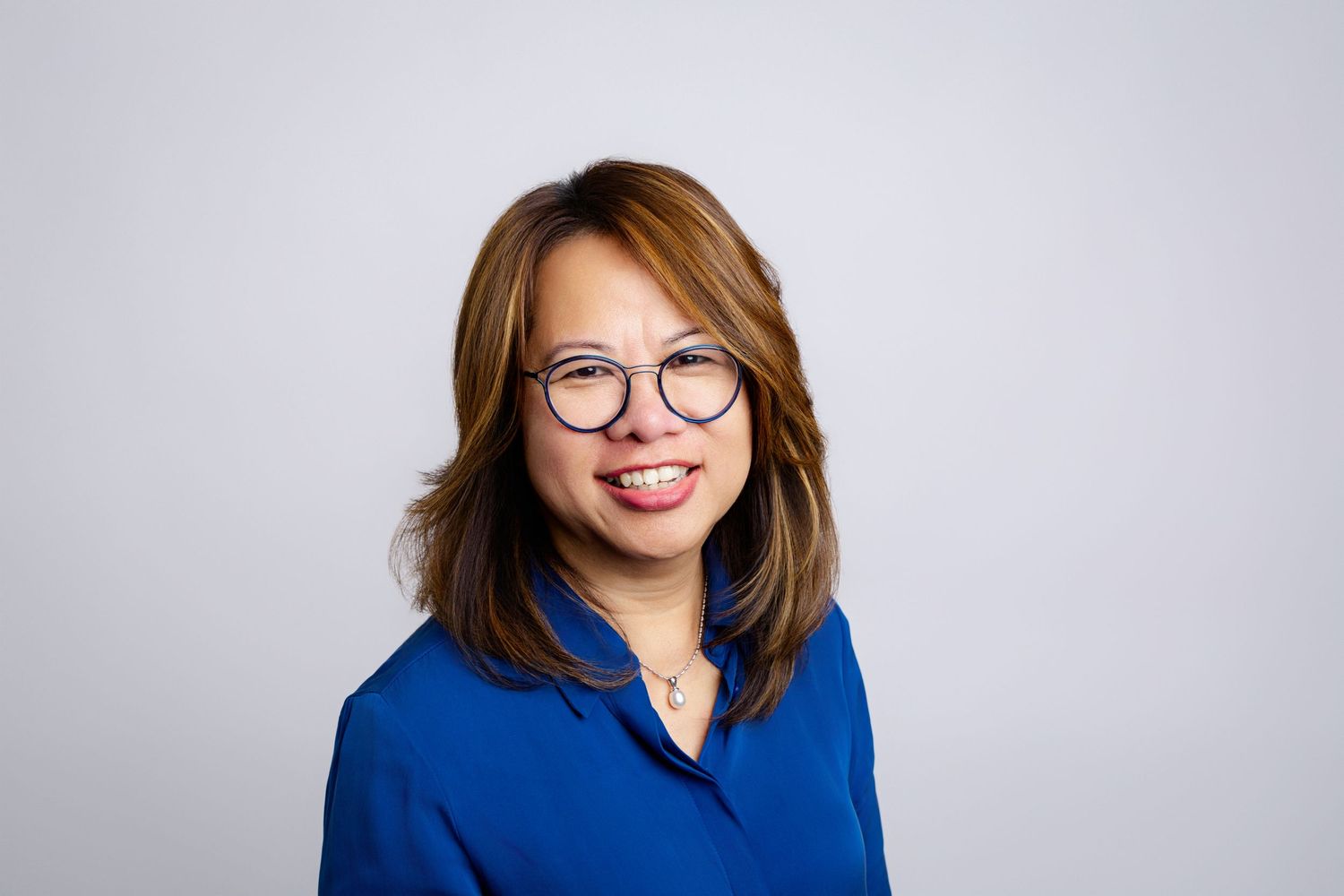 Professional headshot of someone in a blue blazer and glasses against a light gray background.