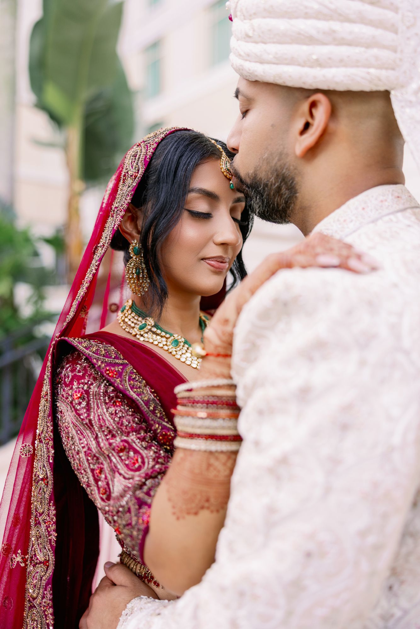 Traditional South Asian wedding couple in elegant red and white attire share intimate moments during their photoshoot.