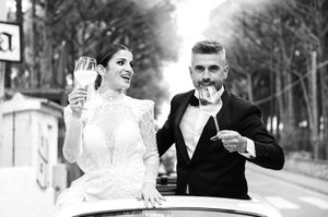 Newlywed couple toasting and celebrating in a vintage car on their wedding day in black and white.