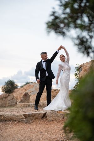 Bride and groom dancing together on rocky terrain against a cloudy sky.