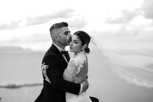 Black and white portrait of newlyweds embracing on a hilltop.