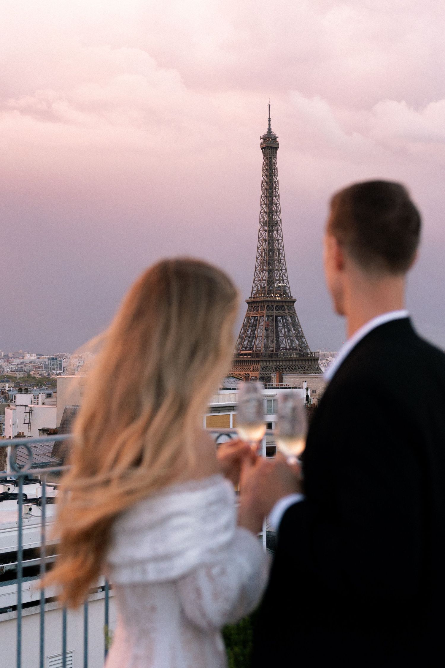 A couple takes photos of the Eiffel Tower from a rooftop terrace during sunset in Paris.