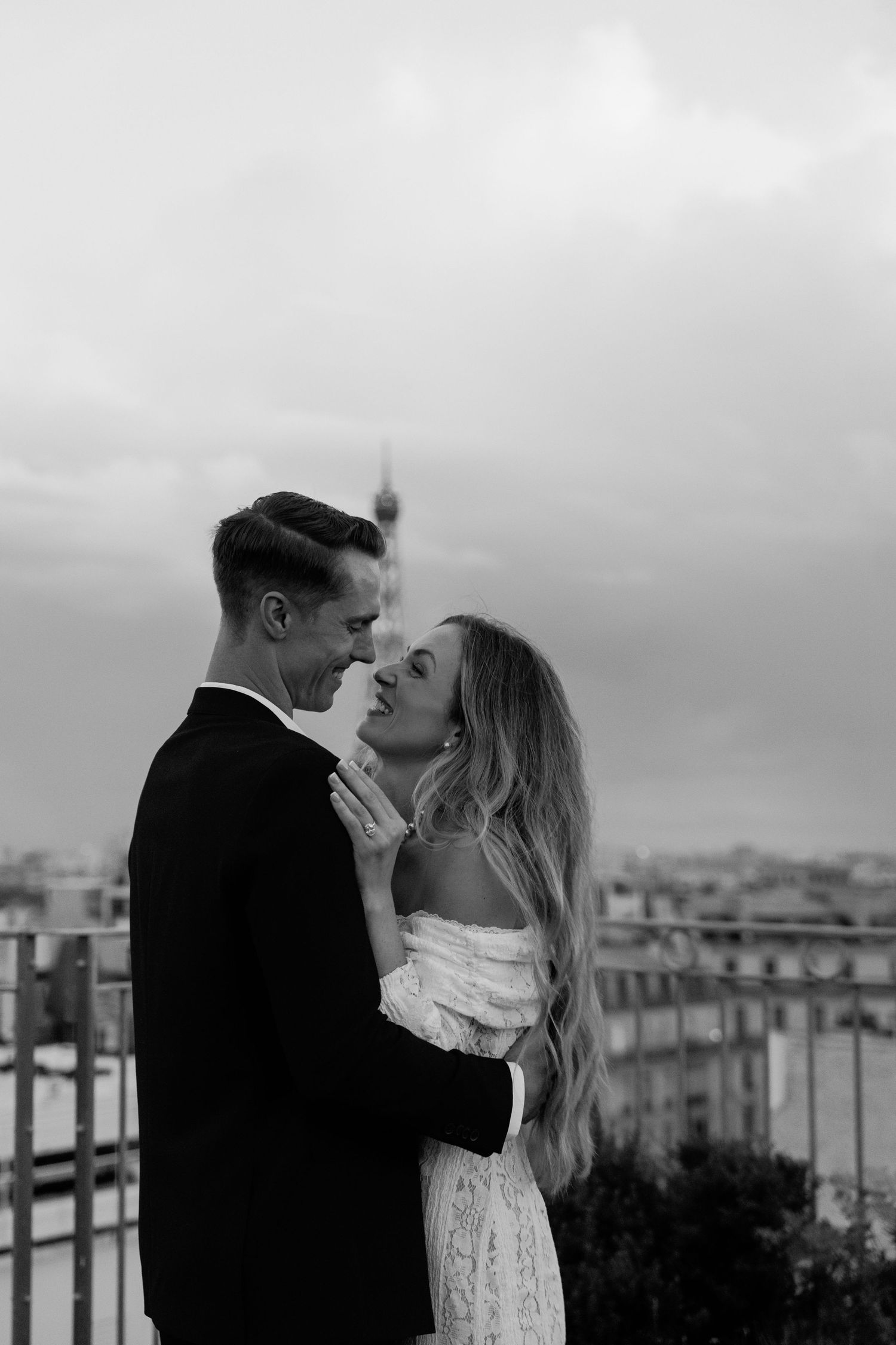 A romantic black and white photo series of a couple sharing intimate moments on a rooftop overlooking a city skyline.