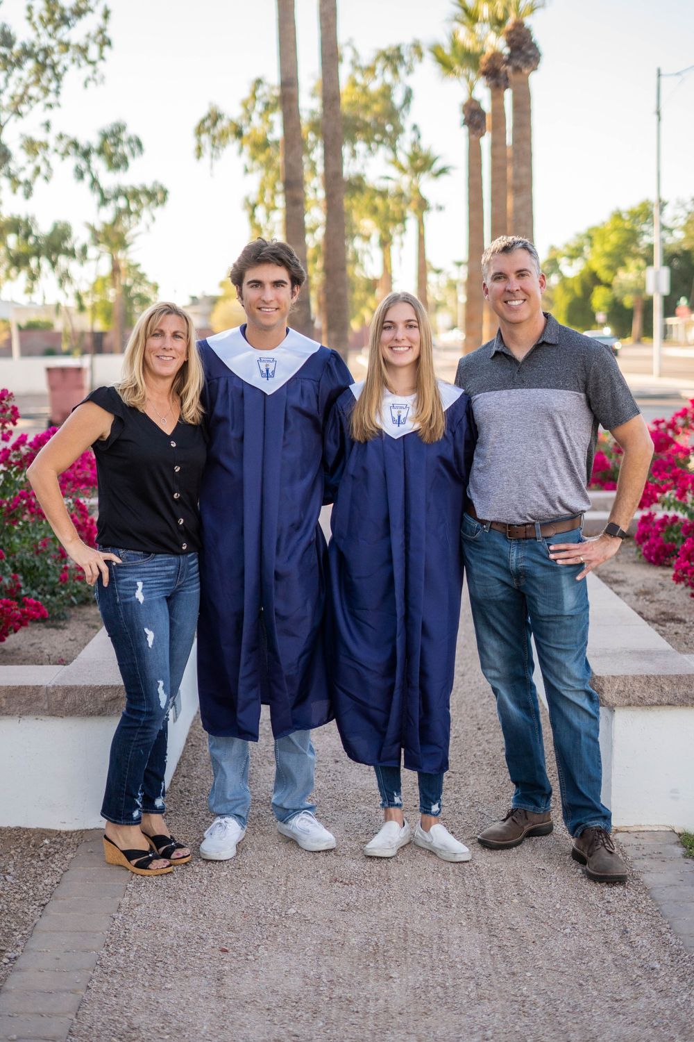 Family photo with graduates in blue caps and gowns standing between parents outdoors.