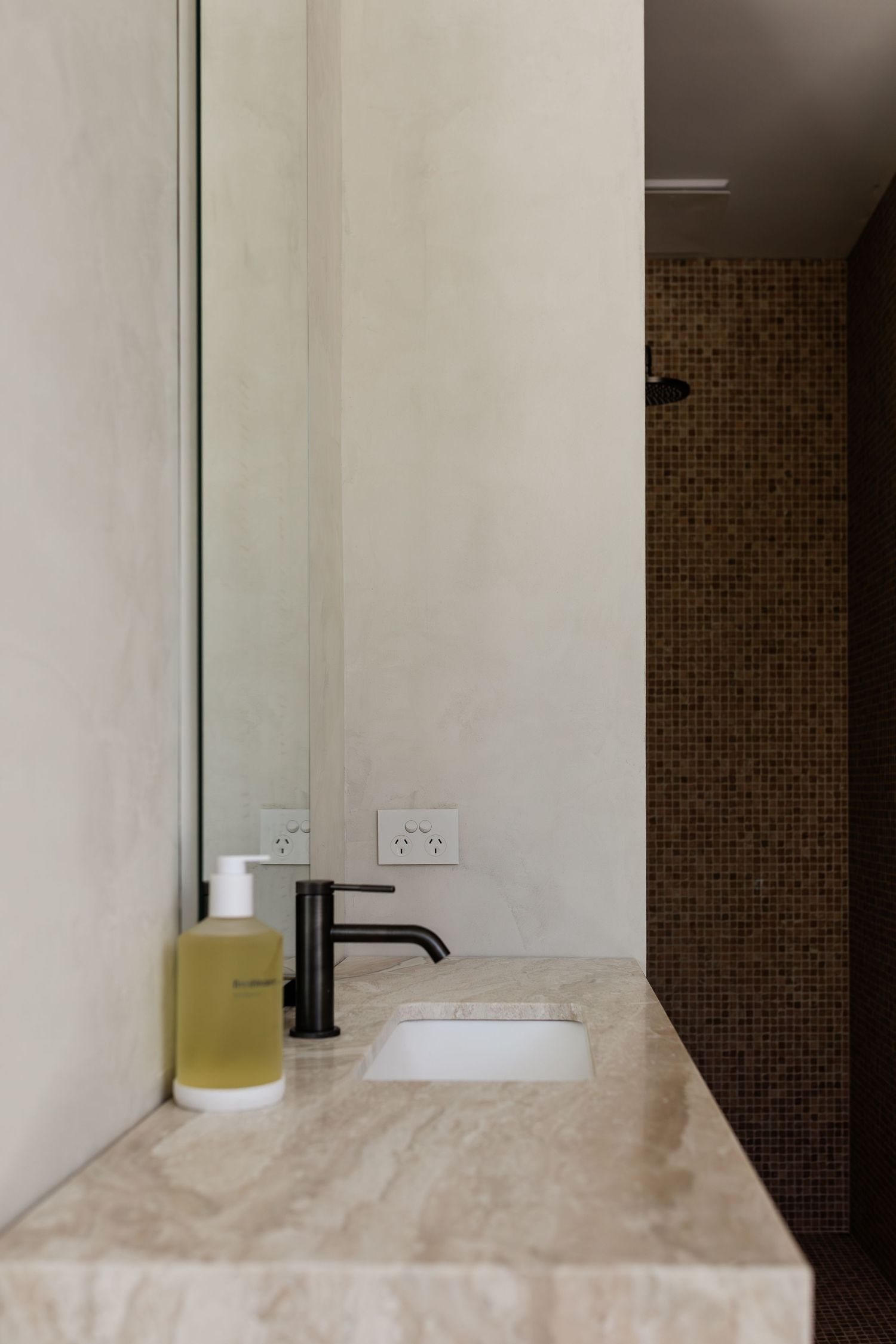 Modern bathroom vanity with white stone countertop, black faucet, and brown mosaic tile backsplash in minimalist style.