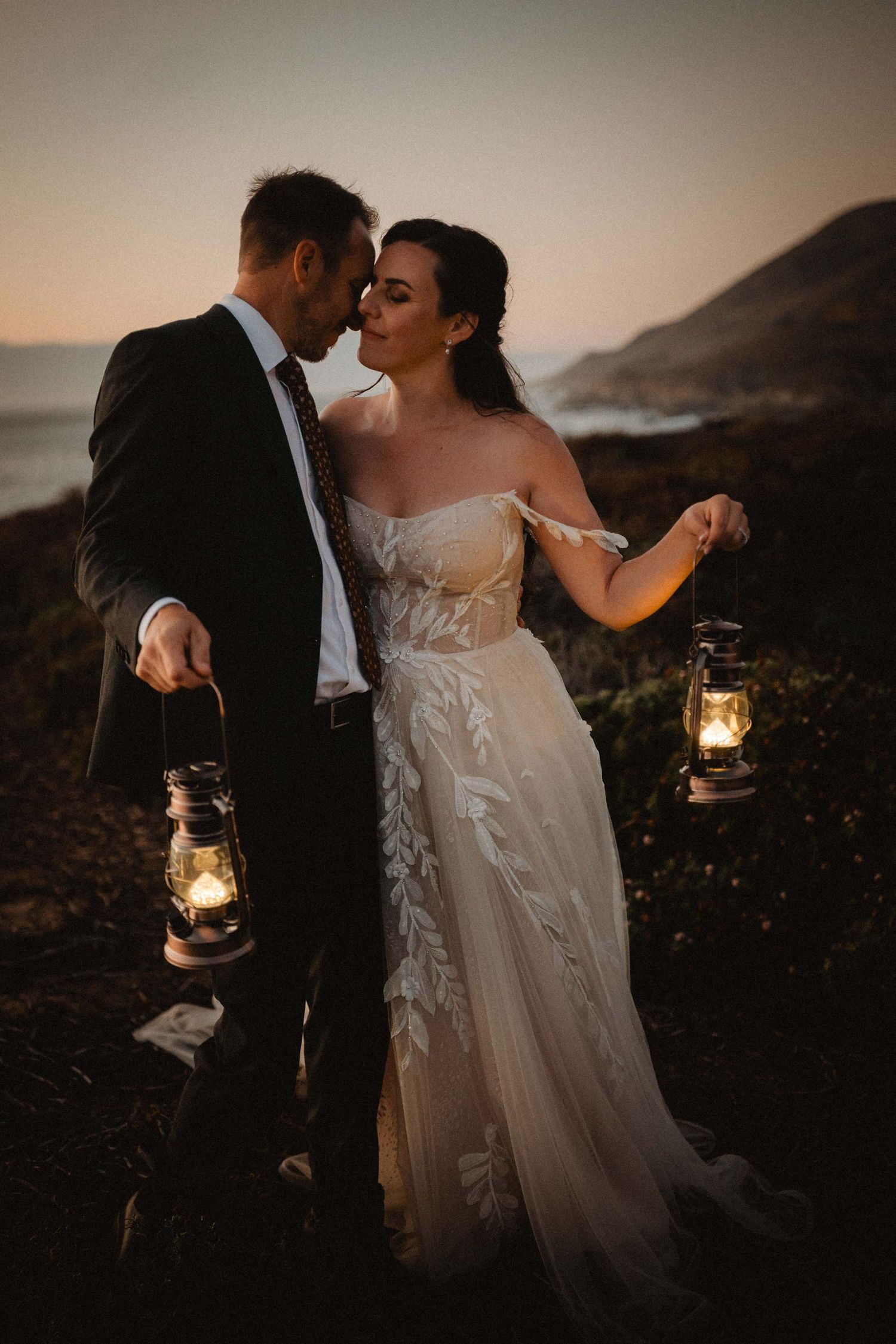 bride and groom holding lanterns during blue hour overlooking the cliffs