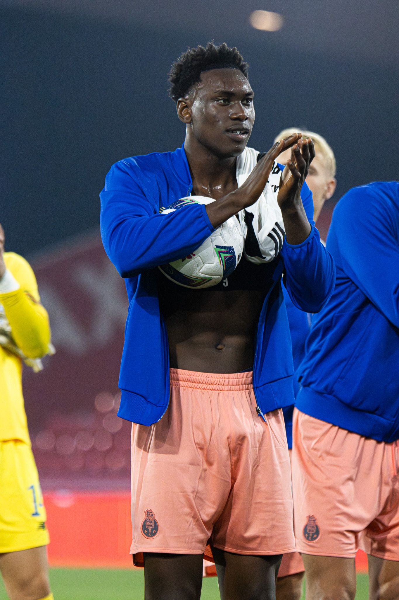 Soccer players in coral jerseys putting on blue jackets after the match.
