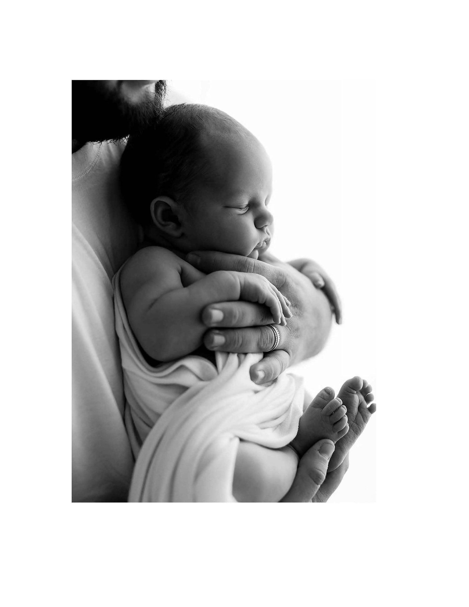 A tender black and white photograph shows a parent cradling a sleeping infant wrapped in soft white fabric.