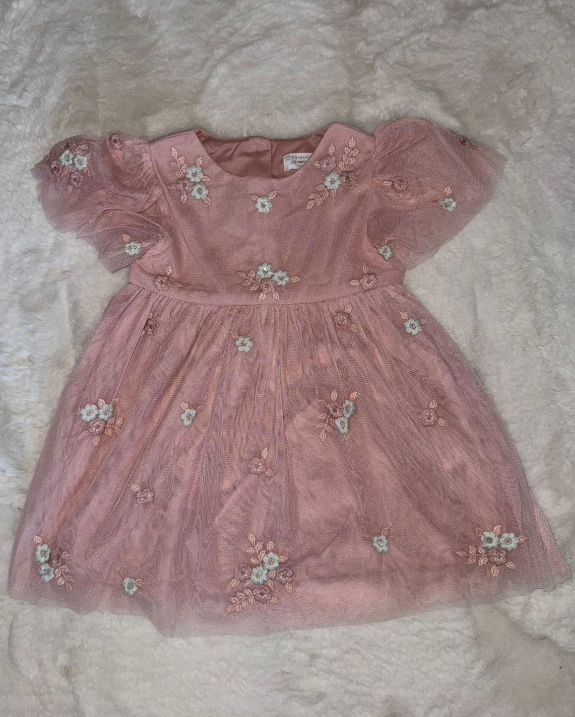 Pink embroidered baby dress with delicate floral details laid flat.
