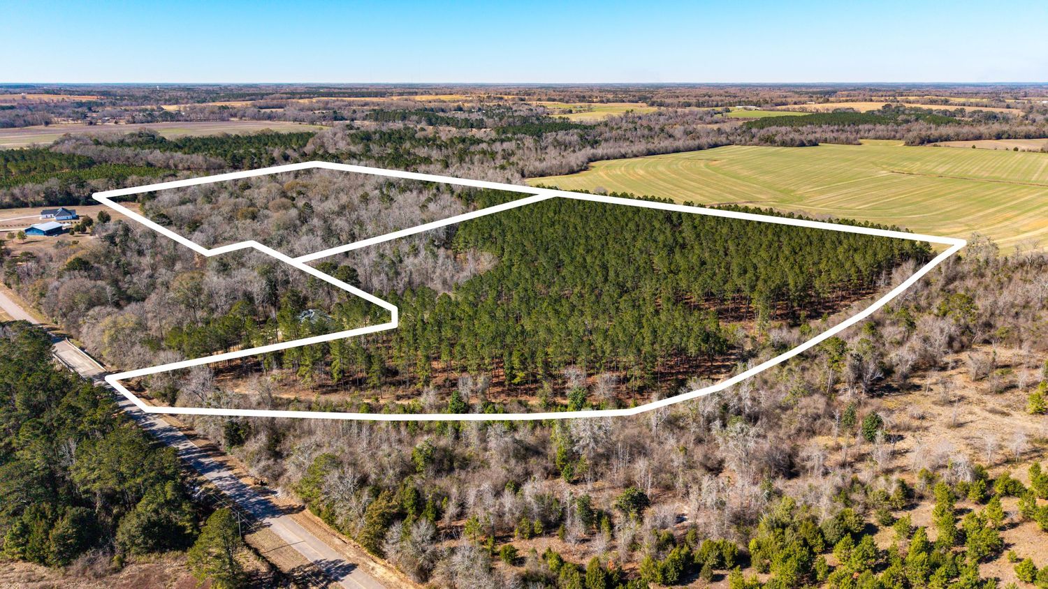 Aerial view of a rural airstrip runway surrounded by farmland and forests stretching into the distance.