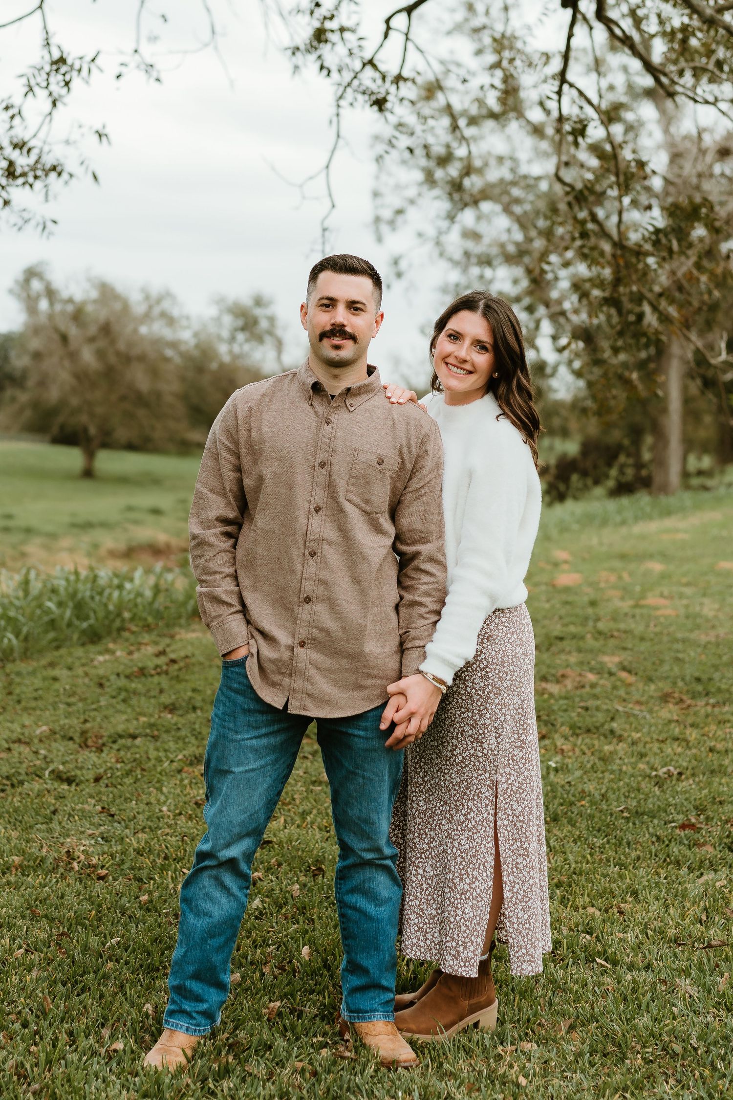 Couple in casual attire poses together on a green hillside during a photo session.