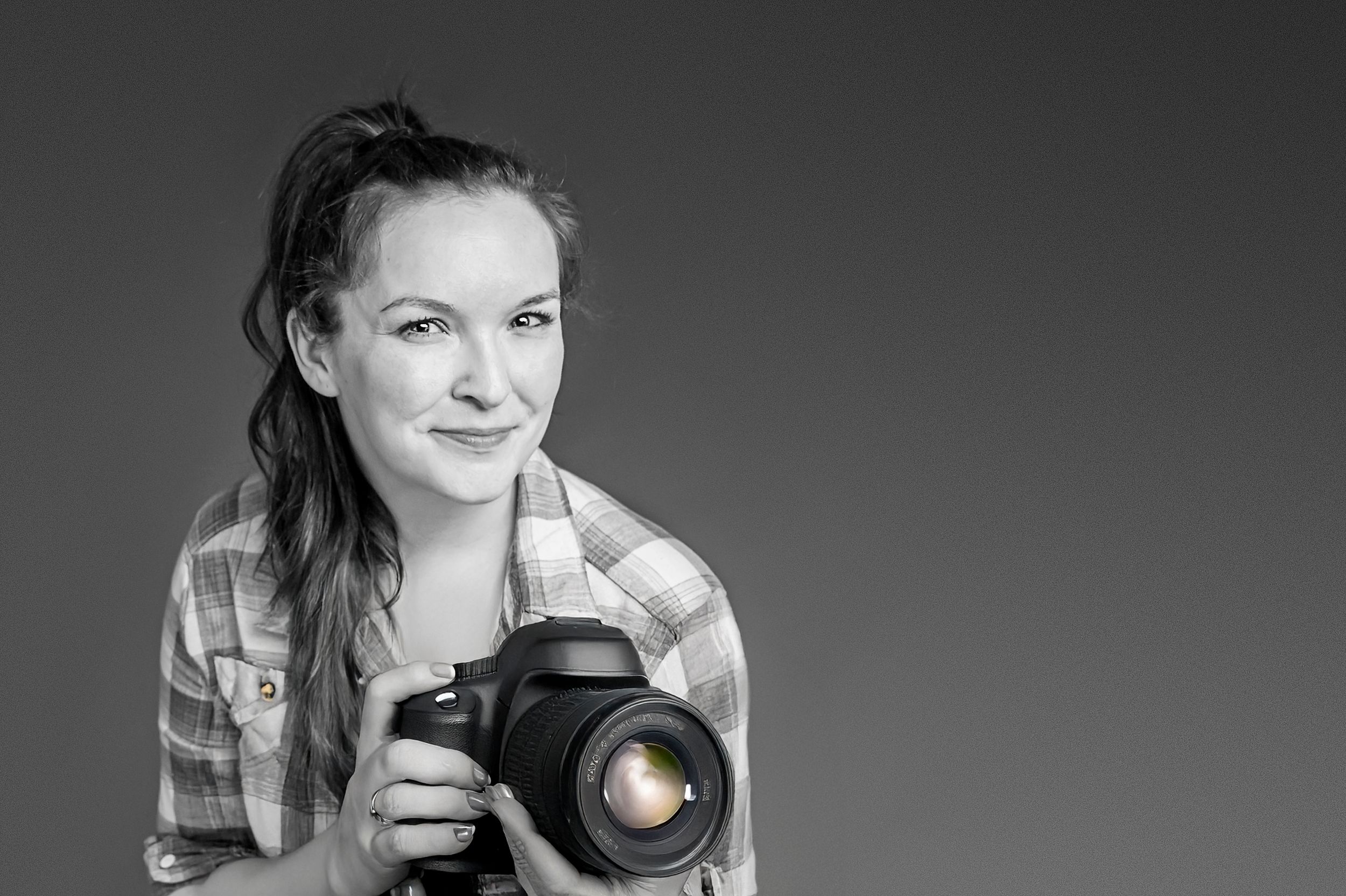 A monochromatic portrait of someone holding a professional camera with a bright expression.