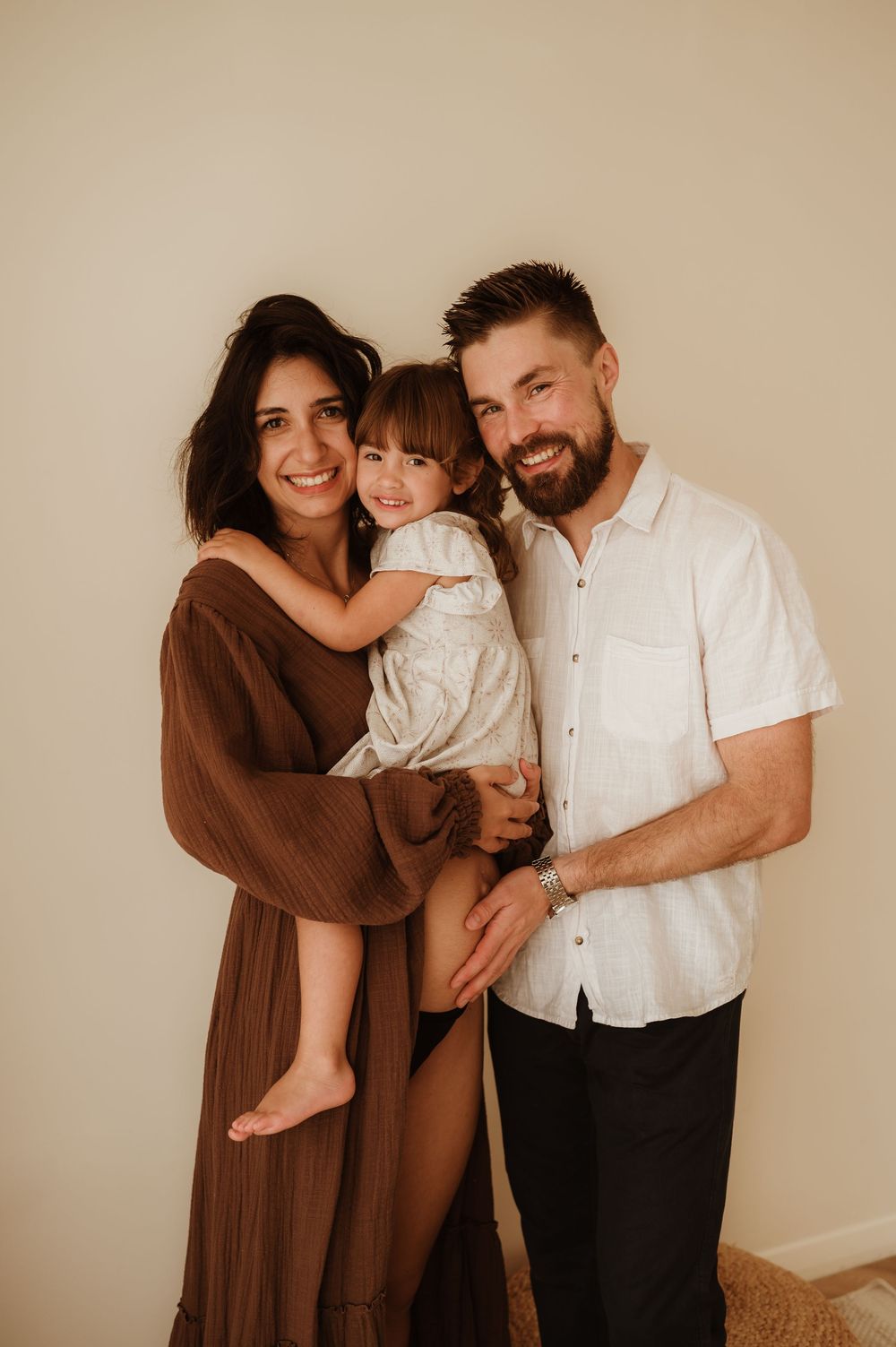 Family wearing brown and white outfits poses together against neutral backdrop in studio portraits.