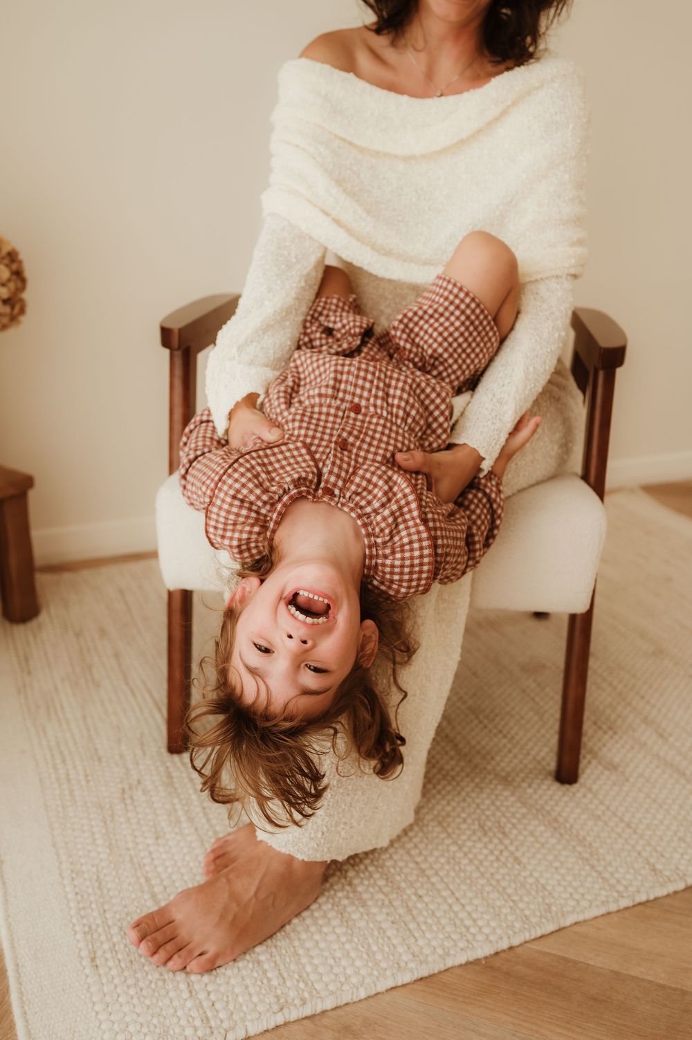 Playful moments shared on a wooden chair against a light backdrop with gingham and knit clothing.