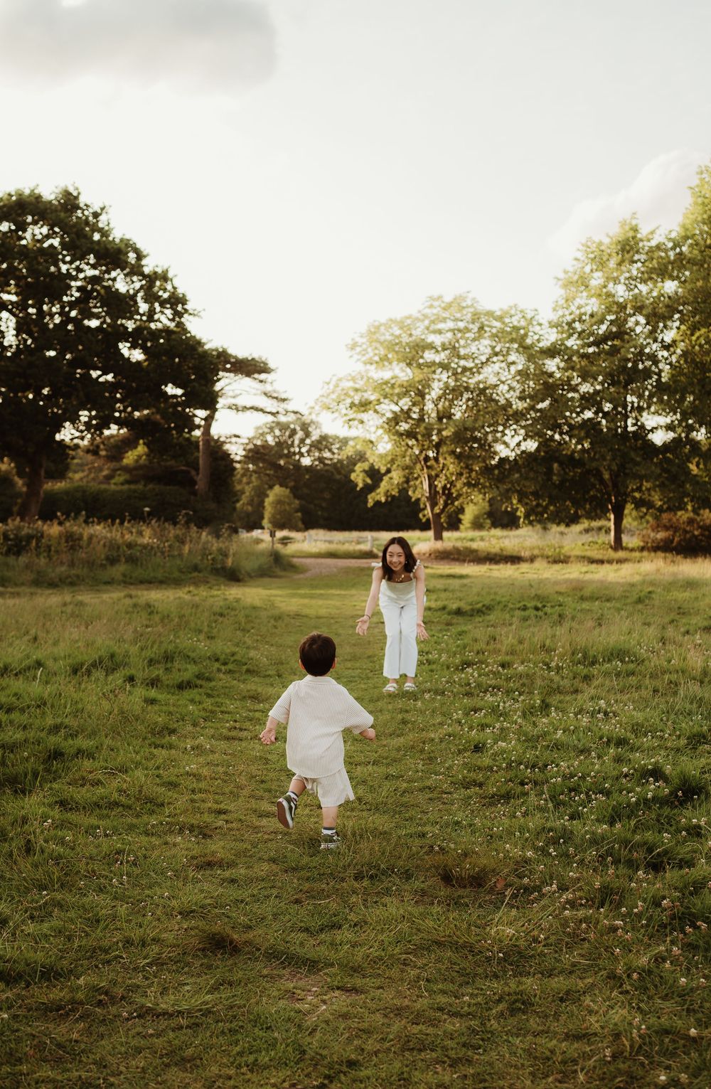 People wearing white dresses stand in a green field during golden hour sunset, creating a dreamy pastoral scene.