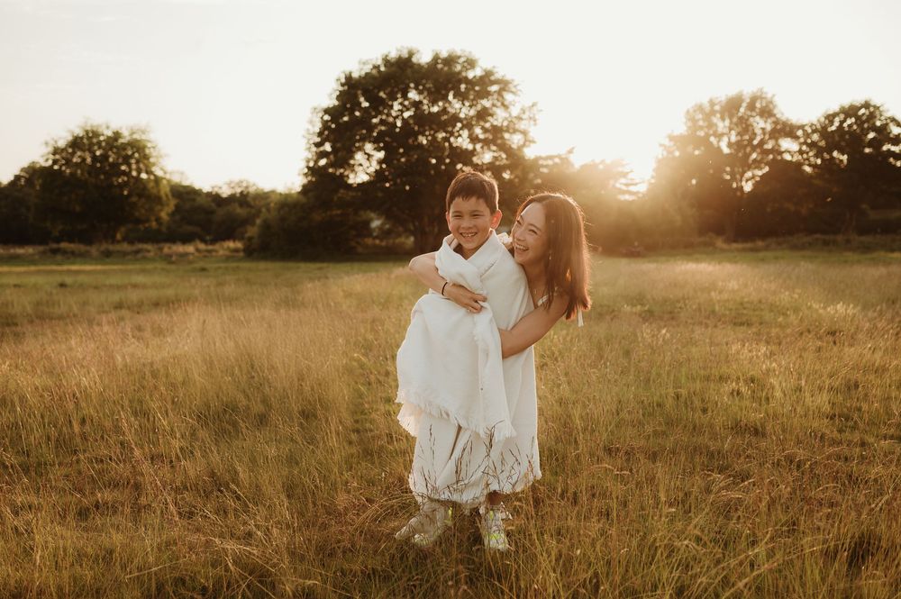 Two figures in white dresses embrace in a golden sunlit meadow during sunset, creating a dreamy summer scene.