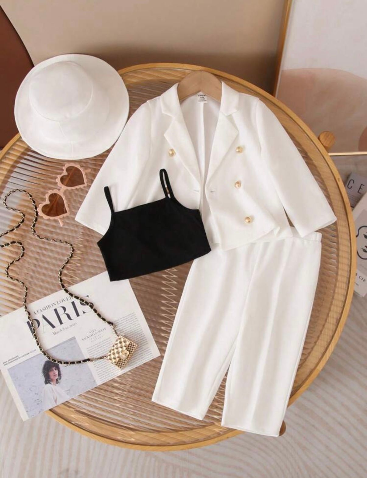 White three-piece outfit set with blazer, black camisole, and pants on wooden tray with accessories.