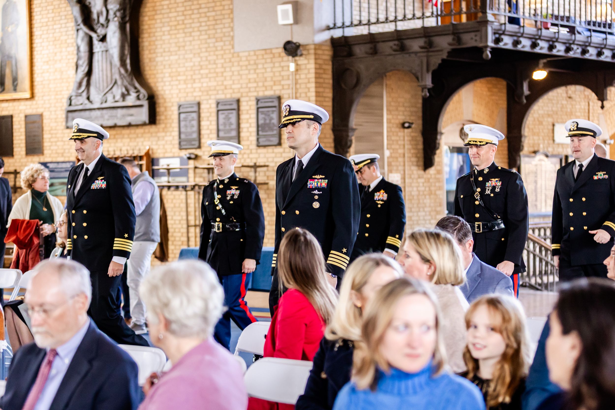 Military service members in dress uniforms stand in formation during a ceremony as crowd gathers in foreground.