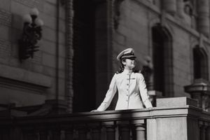 A person in a white suit stands on a balcony or terrace against a stone building in black and white photography.