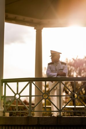 Silhouette of a Naval officer standing at a railing during golden hour sunset with columns in background.
